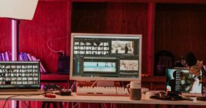 A video editing workstation with a timeline and clip bins open across a monitor and laptop in a studio