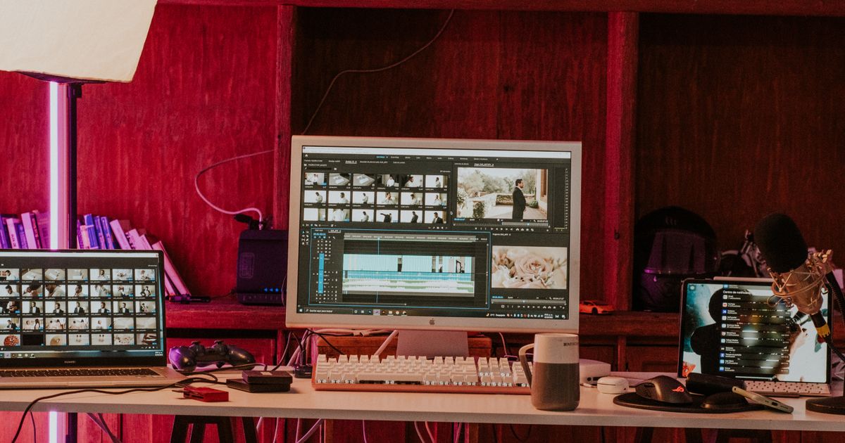 A video editing workstation with a timeline and clip bins open across a monitor and laptop in a studio