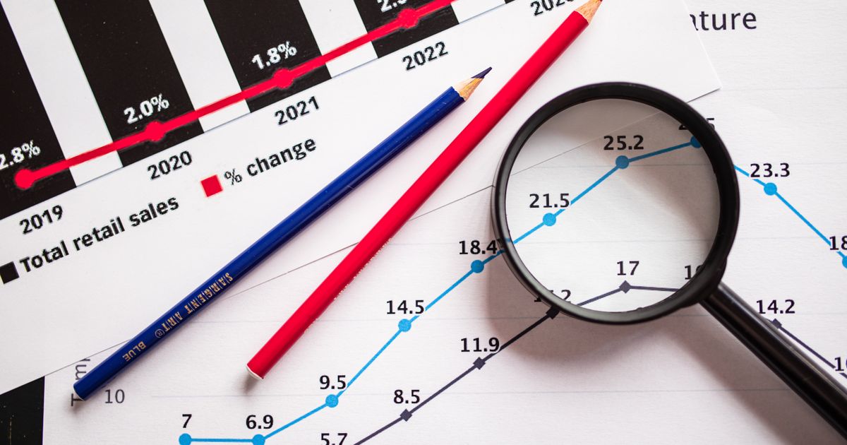 Magnifying glass and coloured pencils resting on printed sales charts, illustrating an audit of website conversion figures