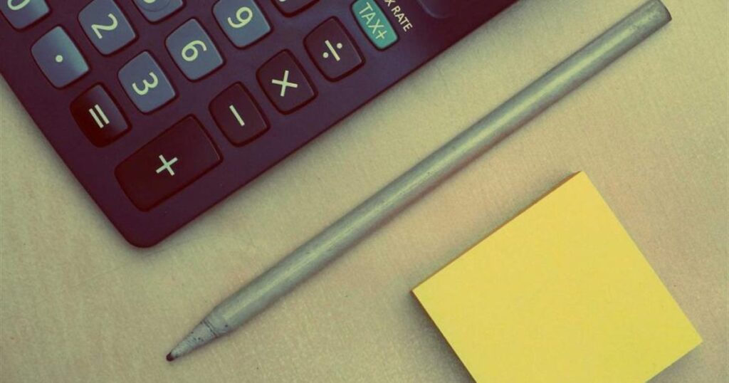 Calculator, pencil and a blank sticky note on a desk, used for working out a website budget