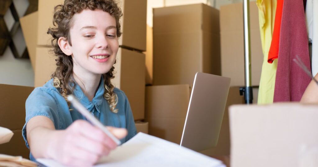 Small business owner writing notes beside a laptop and stacked parcels while running an online store