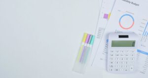 Monthly budget worksheet with a bar chart, a calculator and coloured pens laid out on a white desk