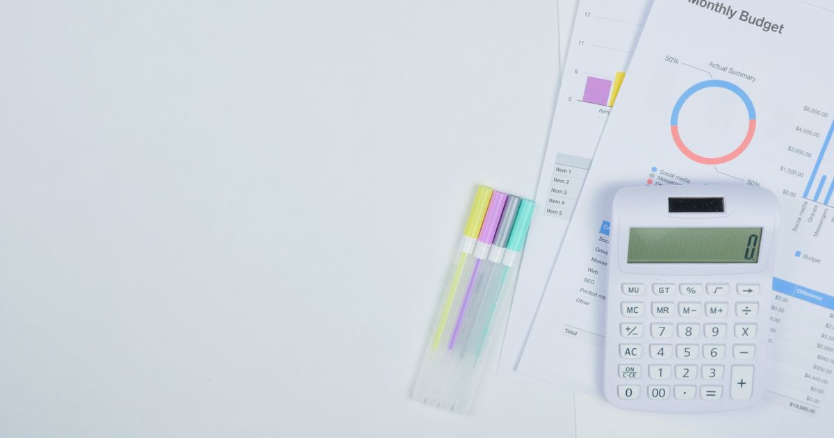 Monthly budget worksheet with a bar chart, a calculator and coloured pens laid out on a white desk