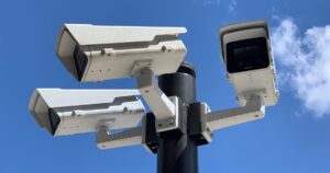 Three security cameras mounted on a pole against a blue sky, used to illustrate monitoring for brand impersonation online