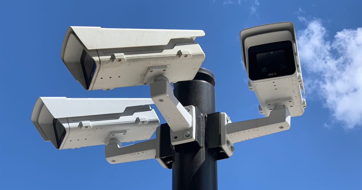 Three security cameras mounted on a pole against a blue sky, used to illustrate monitoring for brand impersonation online
