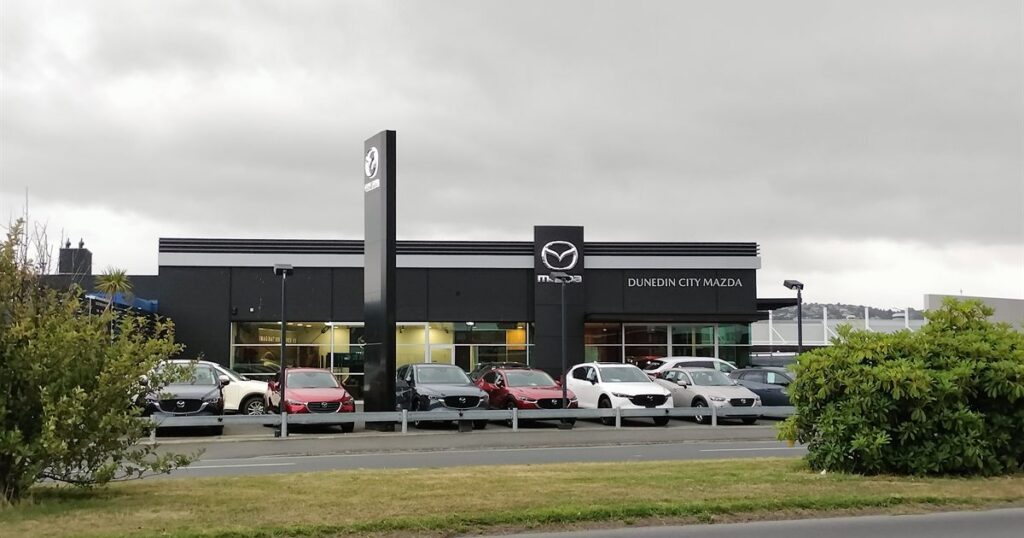 Cars lined up outside a car dealership showroom under an overcast sky