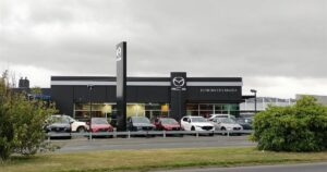Cars lined up outside a car dealership showroom under an overcast sky