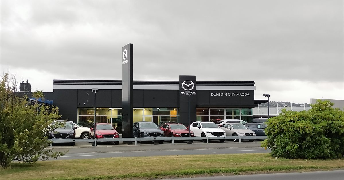 Cars lined up outside a car dealership showroom under an overcast sky