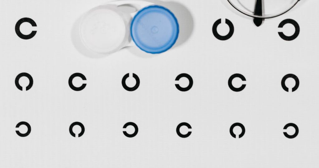 A contact lens case and a pair of spectacles on an eye test chart, illustrating the rules on advertising optical services and contact lenses in Singapore.