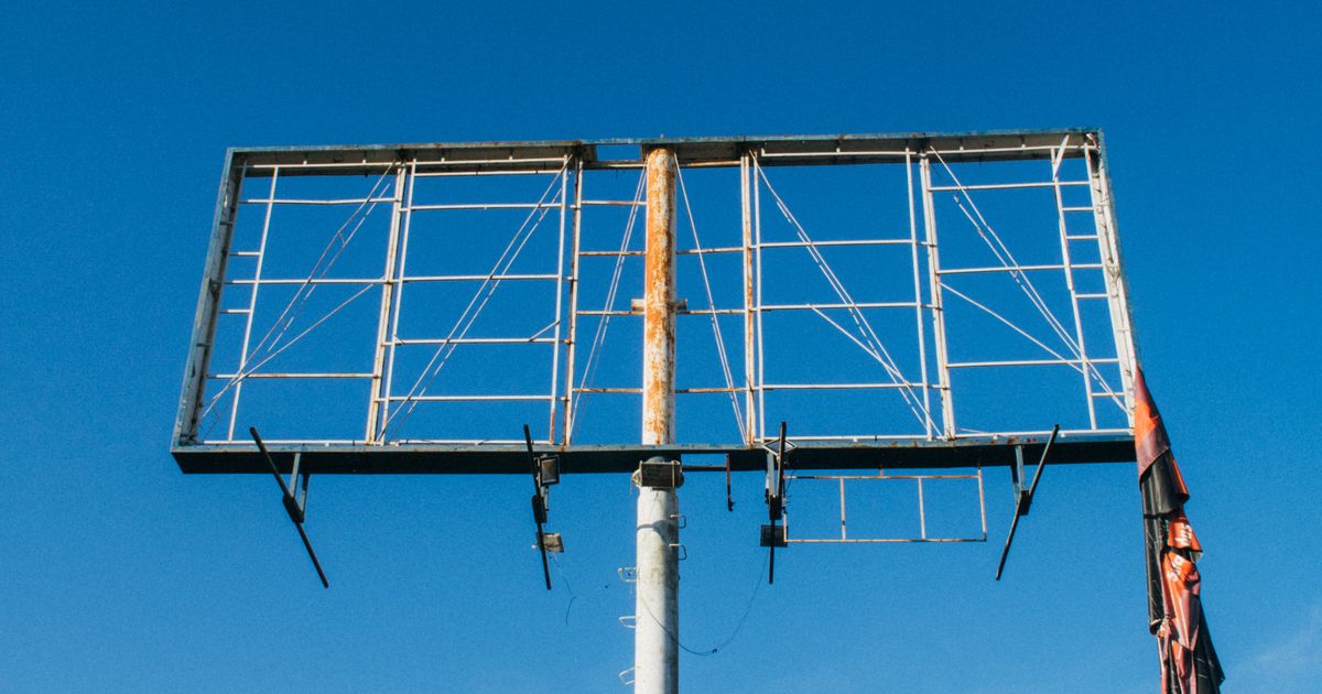 An empty billboard frame stripped of its poster standing against a clear blue sky