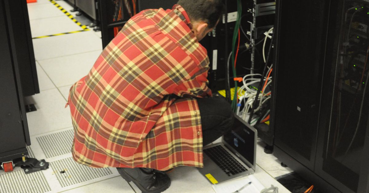 A technician with a laptop working on a server rack in a data centre