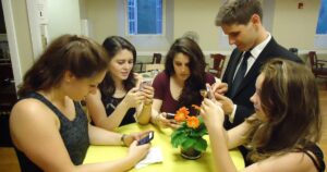 A group of young people sitting together at a table, each looking at their own smartphone