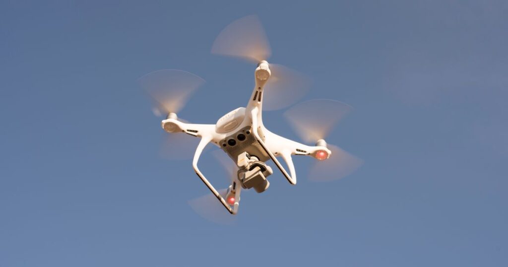 A white camera drone hovering against a clear blue sky, the kind used for aerial marketing video that needs CAAS permits in Singapore.