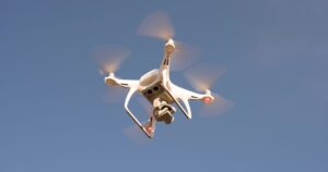A white camera drone hovering against a clear blue sky, the kind used for aerial marketing video that needs CAAS permits in Singapore.