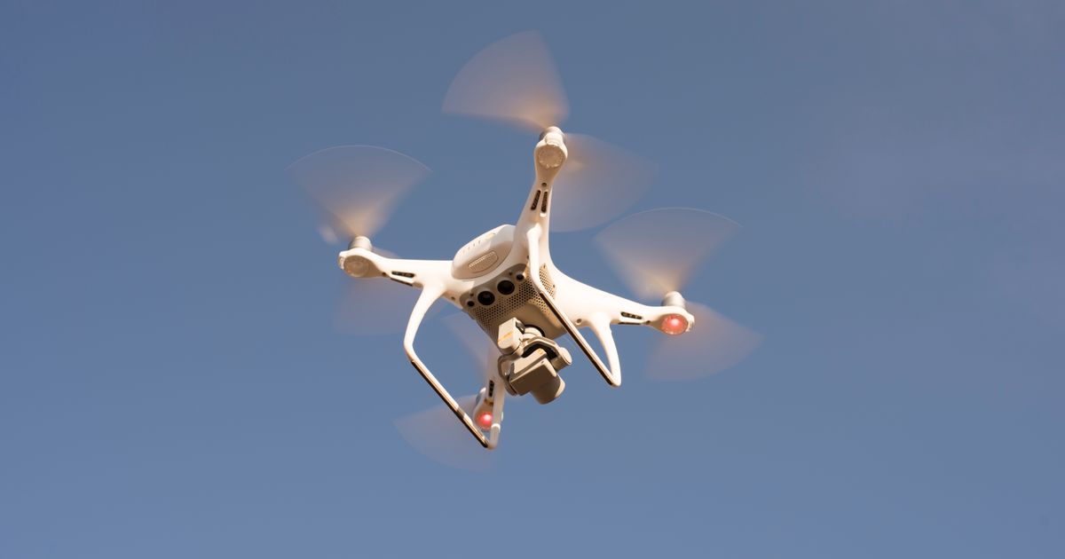 A white camera drone hovering against a clear blue sky, the kind used for aerial marketing video that needs CAAS permits in Singapore.