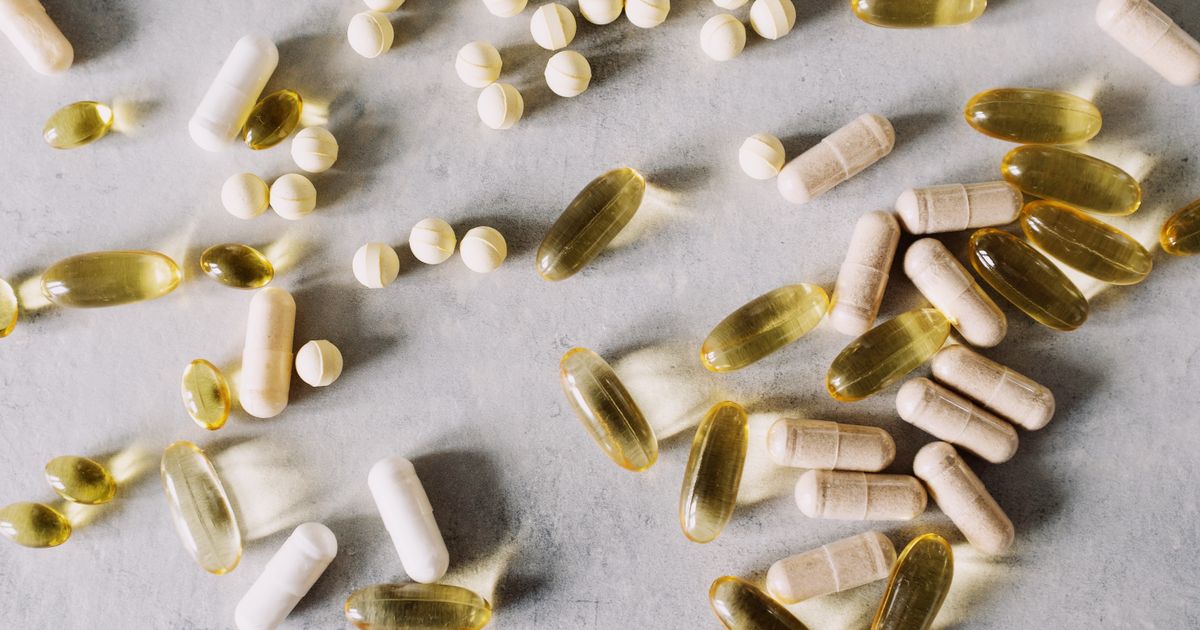 Assorted vitamin softgels tablets and capsules scattered on a pale grey surface