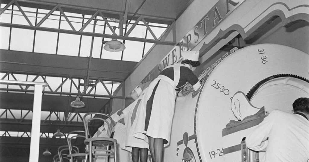 A large numbered sweepstake drum being operated under supervision at a public prize draw