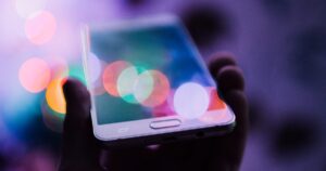 Hand holding a smartphone at night, the screen lit against blurred city lights