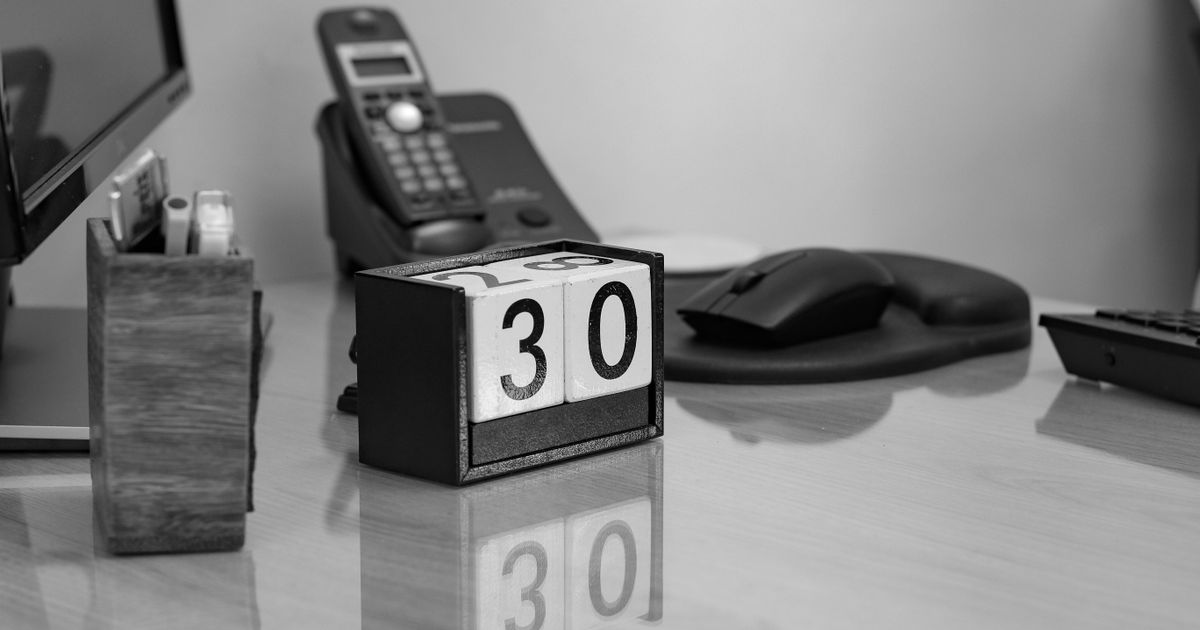 A wooden block desk calendar showing the date 30 on an office desk, in black and white.