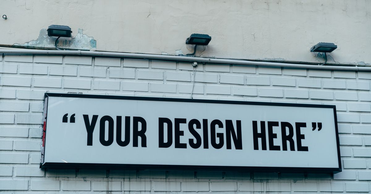 A blank white signboard mounted on a painted brick wall under three floodlights, the kind of outdoor sign that needs a licence in Singapore.
