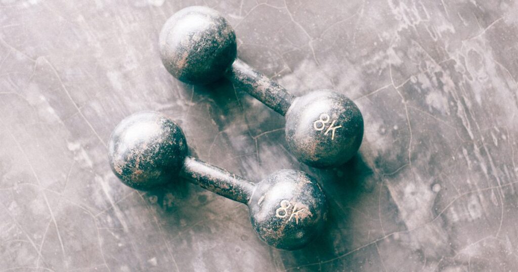 A pair of worn 8 kg iron dumbbells on a grey concrete floor, illustrating gym and fitness packages sold in advance in Singapore.