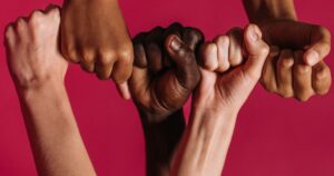 Four arms of different skin tones linking fists against a deep red background, symbolising racial harmony.