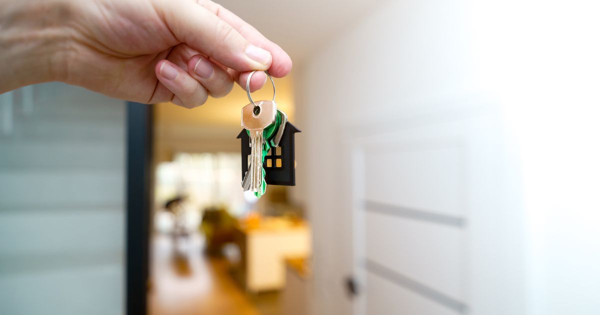 A hand holding a set of house keys on a house-shaped keyring inside a bright apartment, illustrating the rules on advertising rentals in Singapore.