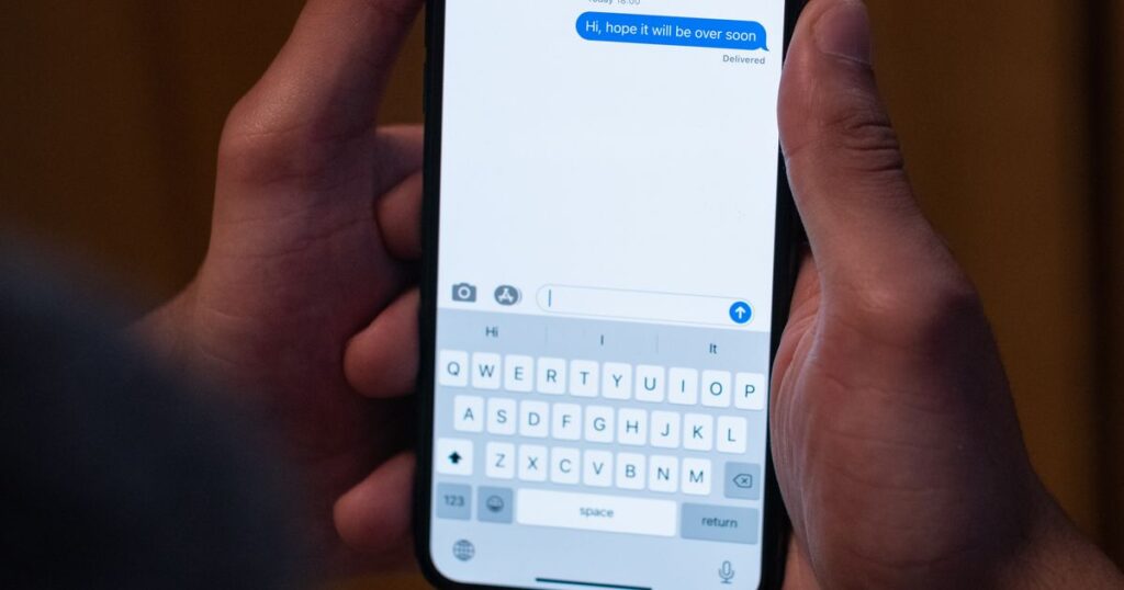 Close-up of two hands holding a smartphone with a text message conversation open on screen