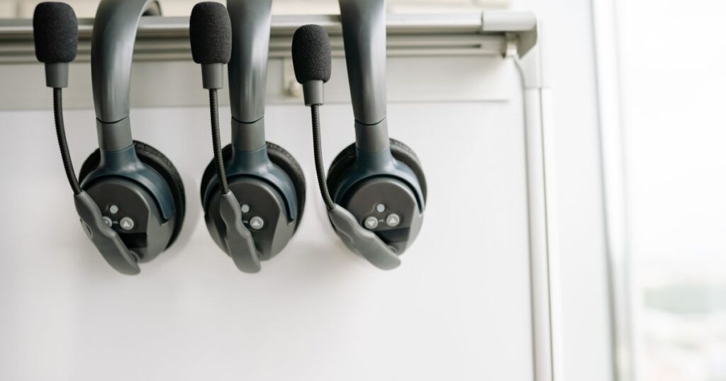Three call centre headsets with boom microphones hanging on a rail in front of a whiteboard