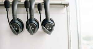 Three call centre headsets with boom microphones hanging on a rail in front of a whiteboard
