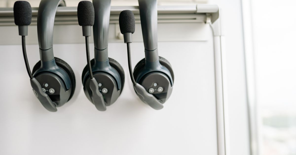 Three call centre headsets with boom microphones hanging on a rail in front of a whiteboard