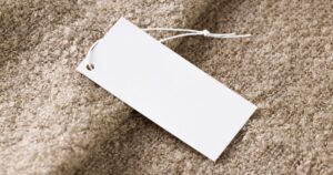 A blank white hang tag on a beige boucle fabric, representing the product labels and descriptions regulated in Singapore.