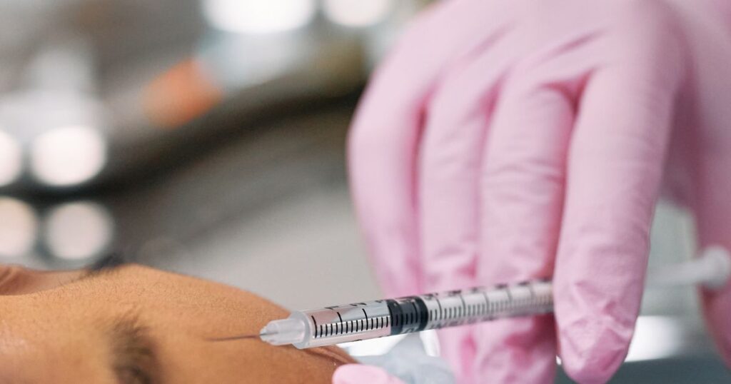 A gloved hand holding a fine syringe during a cosmetic injection, illustrating the advertising rules for aesthetic clinics and beauty salons in Singapore.