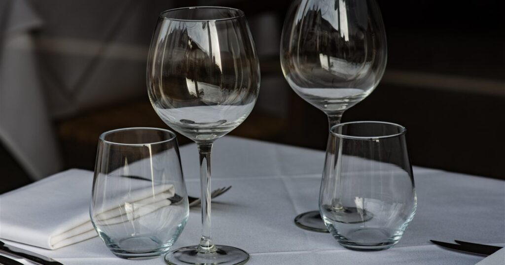 Empty wine glasses and tumblers on a white tablecloth at a restaurant table, illustrating the rules on advertising and marketing alcohol in Singapore.