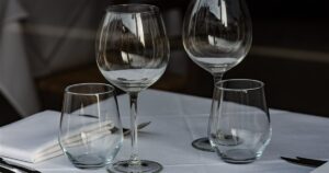 Empty wine glasses and tumblers on a white tablecloth at a restaurant table, illustrating the rules on advertising and marketing alcohol in Singapore.
