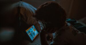A child in a dimly lit room looking at a glowing tablet screen, illustrating the PDPA rules for collecting children's personal data in marketing in Singapore.
