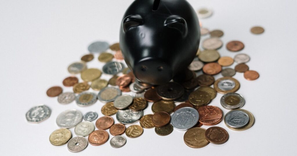 A black piggy bank standing on a scatter of coins on a white surface, illustrating the rules on advertising deposit and savings promotions in Singapore.