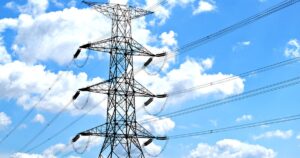 A steel electricity transmission tower carrying high-voltage lines against a blue sky with white clouds, illustrating the rules on marketing electricity plans in Singapore.