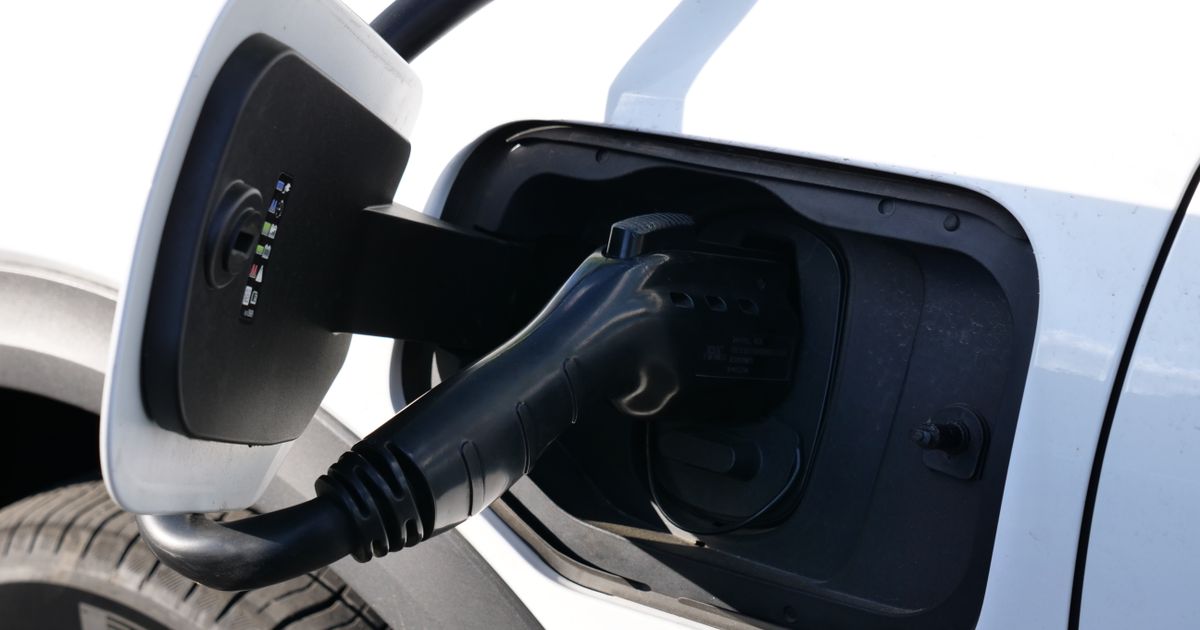 A black charging connector plugged into the charging port of a white electric car, illustrating the rules on advertising EV chargers in Singapore.