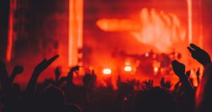 Silhouetted concert crowd with raised hands in front of a stage washed in red light, illustrating the licensing and publicity rules for marketing public events in Singapore.
