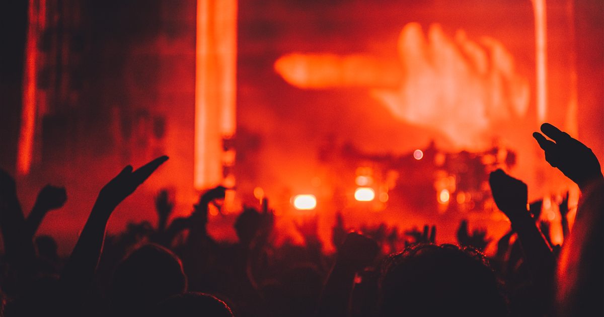 Silhouetted concert crowd with raised hands in front of a stage washed in red light, illustrating the licensing and publicity rules for marketing public events in Singapore.