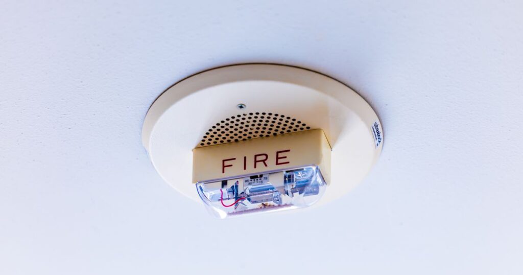 A ceiling-mounted fire alarm with a strobe light and the word FIRE, illustrating the certification rules for selling and advertising regulated fire safety products in Singapore.