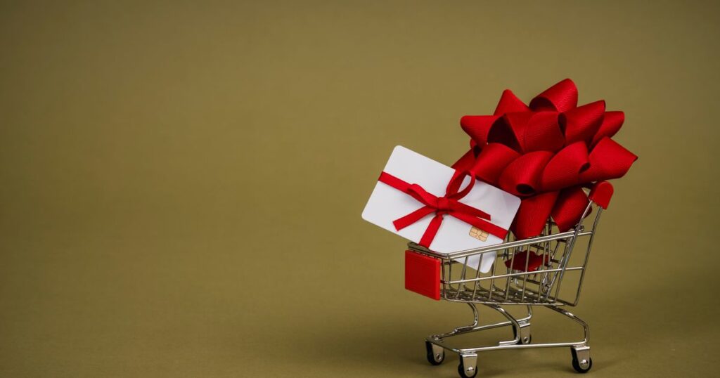 A blank white gift card tied with a red ribbon in a miniature shopping trolley, illustrating the rules for selling gift vouchers and loyalty points in Singapore.