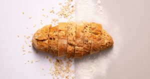 A sliced wholegrain loaf with scattered oats and flour on a white and grey background, illustrating the rules on using the Healthier Choice Symbol in Singapore food marketing.