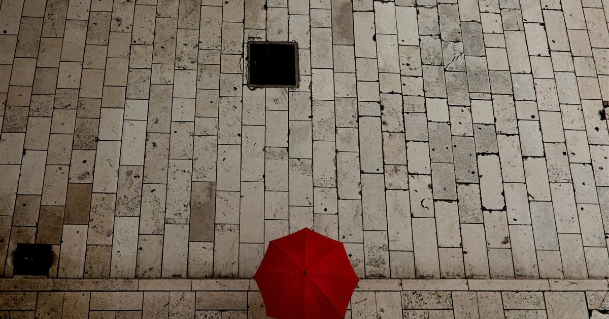 A single red umbrella seen from above on grey stone paving, illustrating protection and the rules on advertising insurance in Singapore.