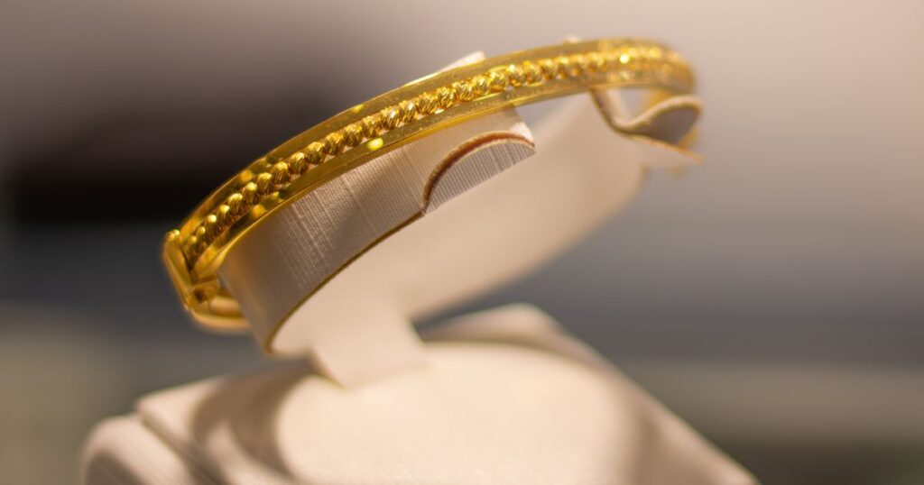 A plain gold bangle with a beaded centre band on a white jewellery display stand, illustrating advertising rules for jewellers and gold sellers in Singapore.
