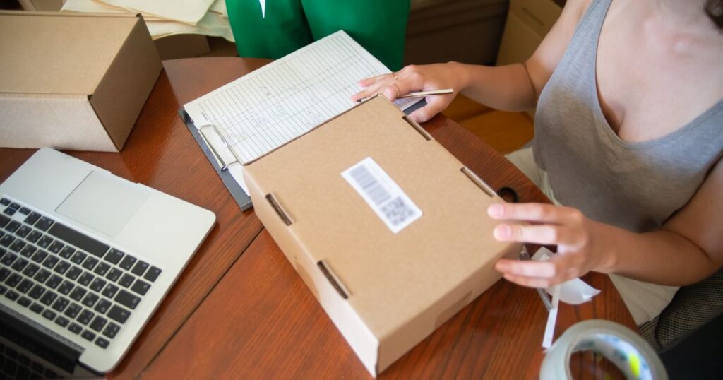 Online seller checking a barcoded parcel beside a laptop while packing orders, illustrating Singapore's marketplace seller verification and anti-scam rules.