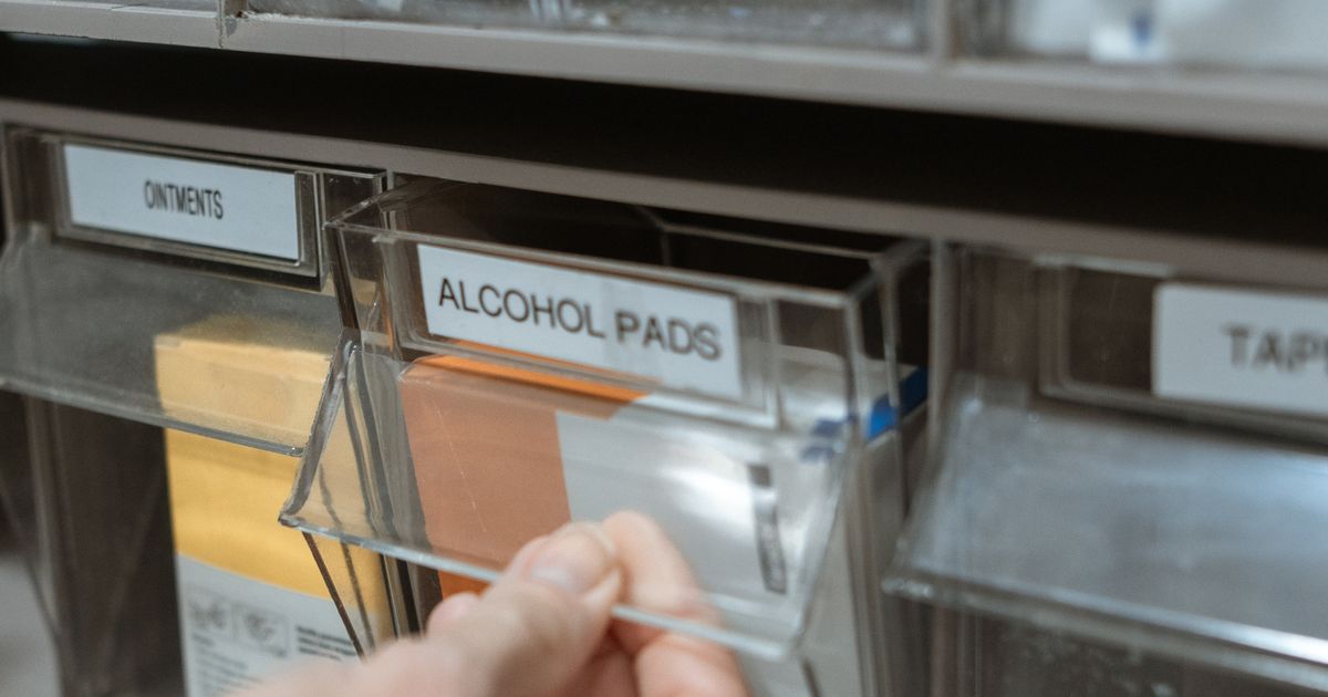 A hand opening a labelled clear drawer of alcohol pads beside ointments in a pharmacy supply cabinet, illustrating the rules on advertising by pharmacies in Singapore.
