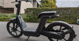 A matte black seated electric scooter parked on an asphalt path beside a hedge, illustrating the rules on selling and advertising e-scooters and PMDs in Singapore.