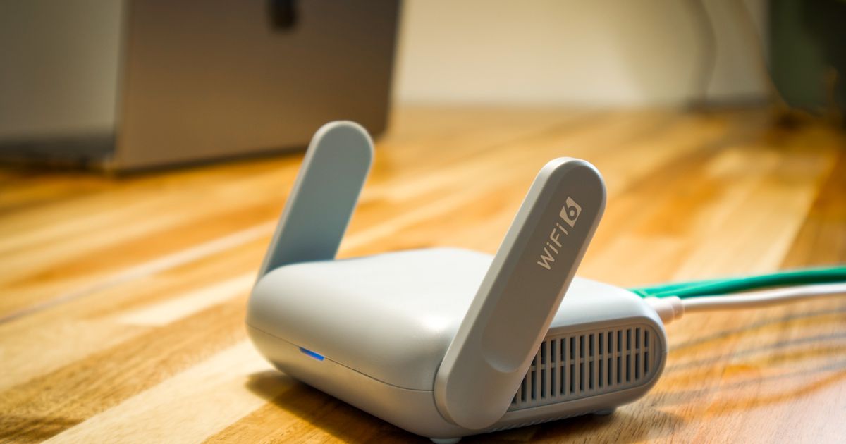 A compact Wi-Fi 6 travel router with two antennas on a wooden desk, illustrating IMDA dealer licensing and advertising rules for selling telecom devices online in Singapore.